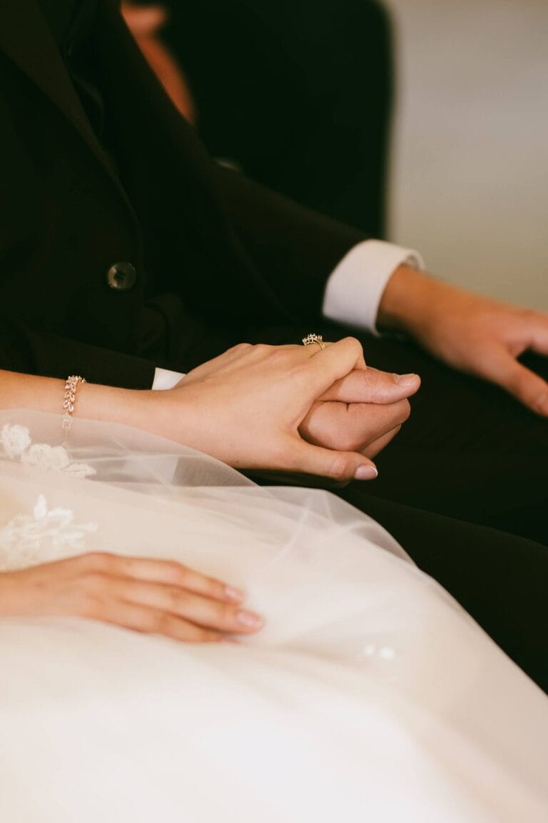 Dłonie pary młodej splecione na tle sukni ślubnej